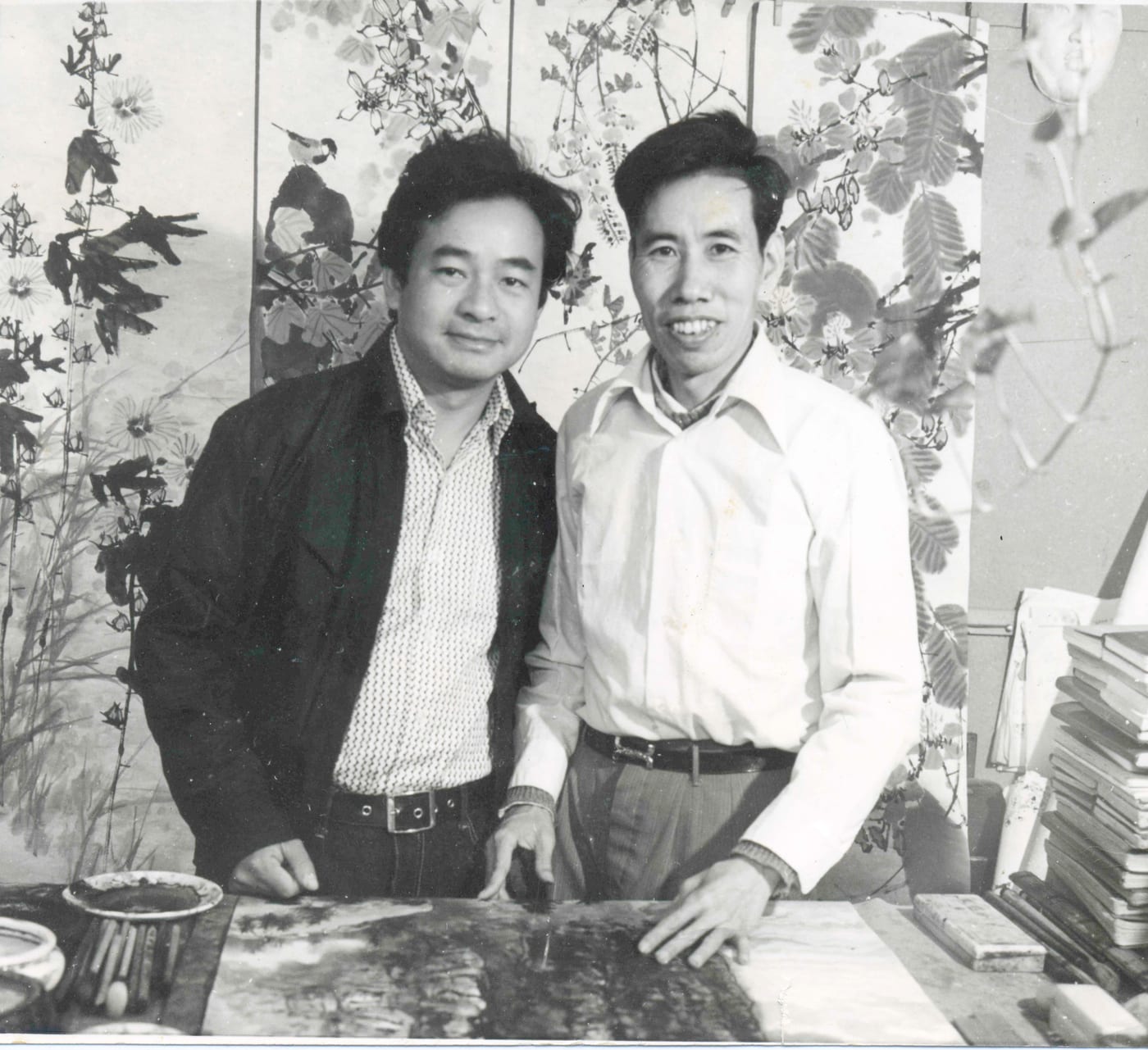 Yim Mau-Kun and Lin Fengsu in a studio, a large ink-painting screen behind them and a painting and brushes on the table